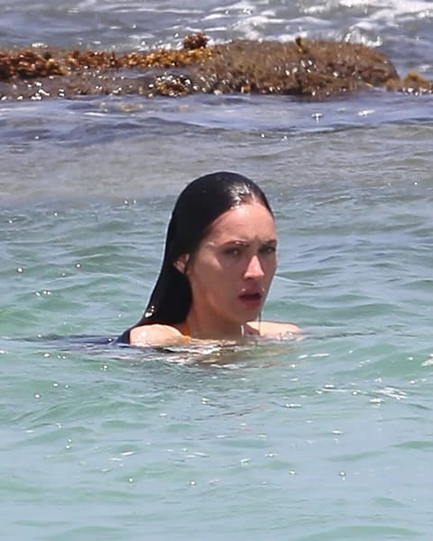 Megan Fox swimming near the rocks on the beach